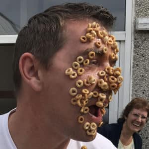 Adult playing game with cheerio breakfast cereal stuck on face