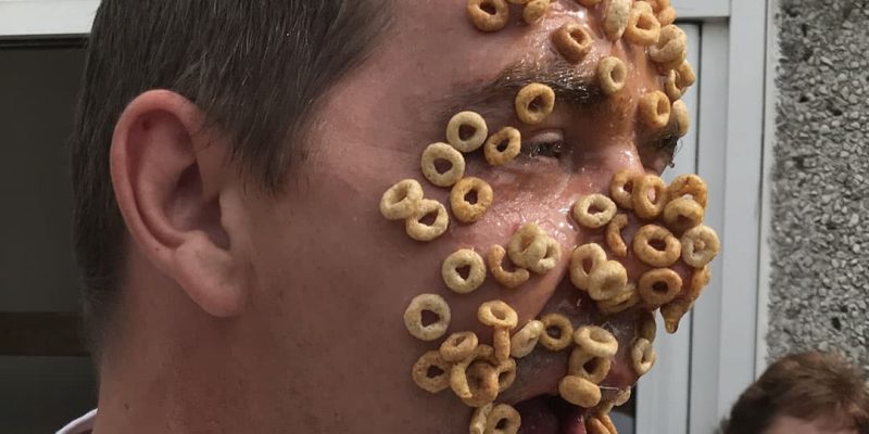 Adult playing game with cheerio breakfast cereal stuck on face
