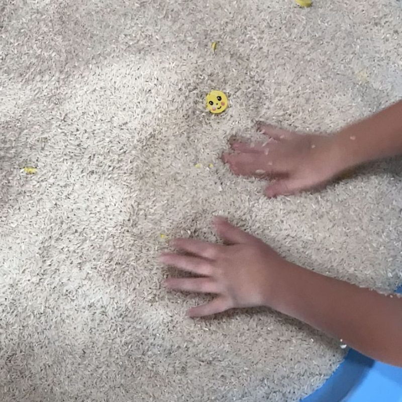 Child's hands playing with rice in a bucket