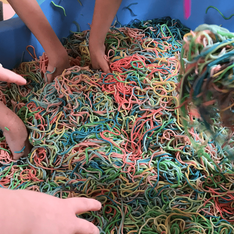 Childrens hands playing in a pool full of multicoloured spaghetti
