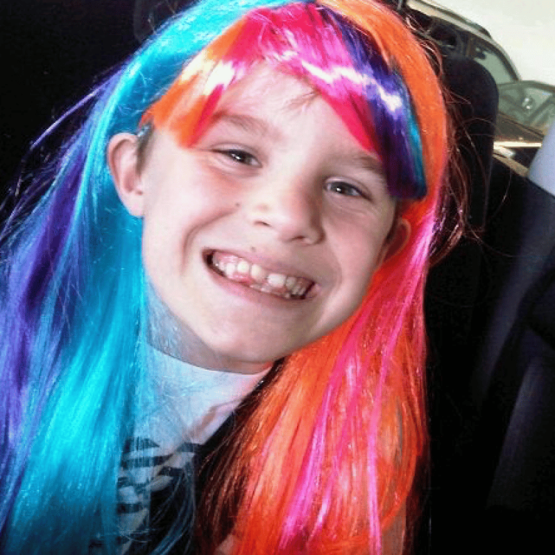 boy wearing a colourful wig smiling at the camera